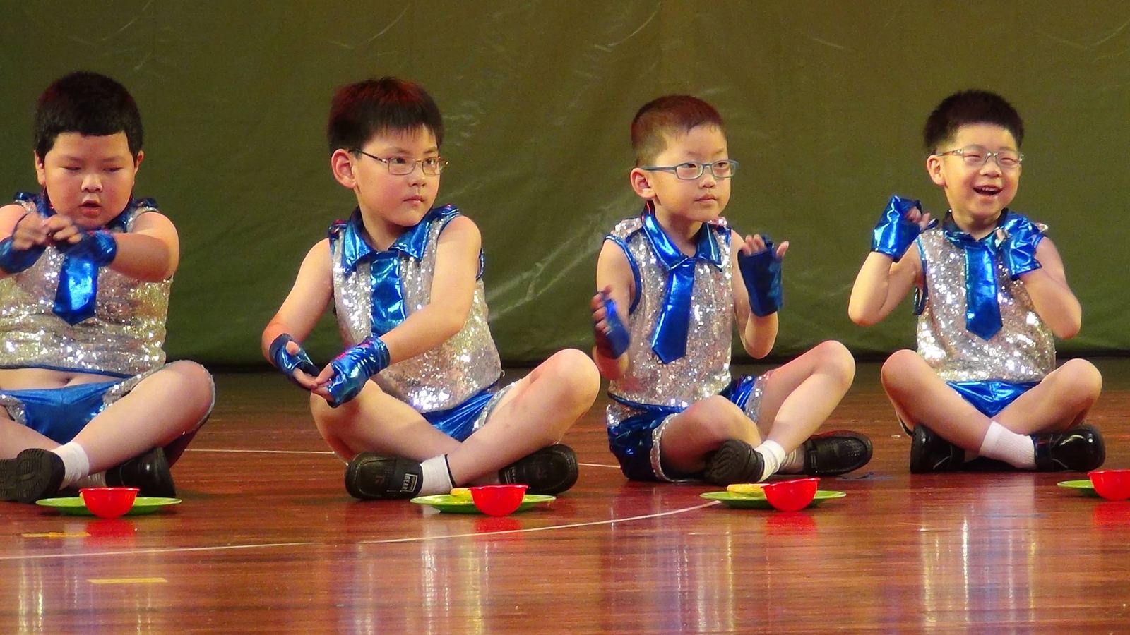 Young performers seated on stage in silver and blue costumes
