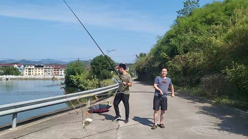 Two people fishing along a riverside road with a net and rods